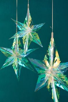 three glass stars hanging from strings against a blue background, one is green and the other is gold