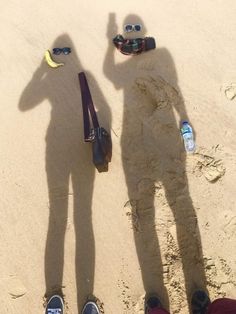 two people standing in the sand with their shadows on them and one person wearing sunglasses