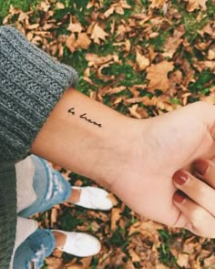 two people holding hands with the word love tattooed on their wrist, in front of leaves