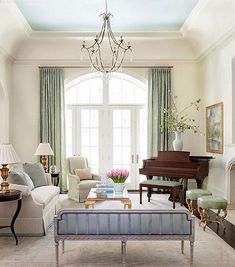 a living room filled with furniture and a chandelier hanging from the ceiling next to a piano