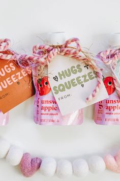 three bags of hugs squeezeze on a white surface with pink and green pom - poms