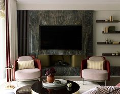 a living room with two chairs and a television mounted on the wall above it's fireplace