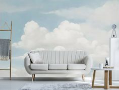 a white couch sitting in front of a blue sky with clouds on the wall behind it