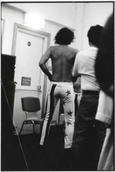 three people standing in front of a door with their back turned to the camera and one person wearing white pants