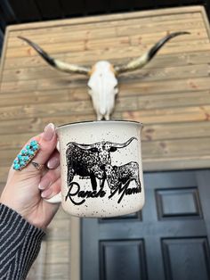 a person holding a coffee cup in front of a cow skull on a wall with long horns