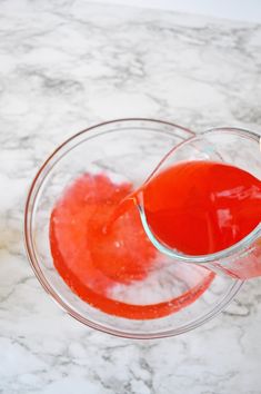 someone is pouring red liquid into a glass on a marble counter top with a spoon