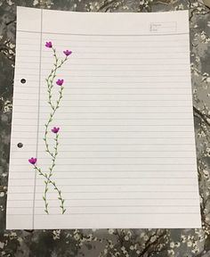 a piece of lined paper with pink flowers on it, sitting on top of a table