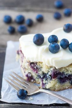 a piece of cake with white frosting and blueberries on top is sitting next to a fork