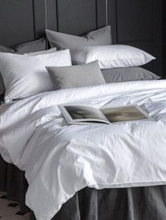 a bed with white sheets and gray pillows