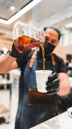 a man in an apron and face mask pouring coffee into a cup