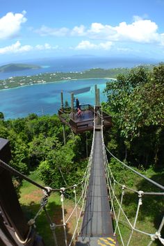 a man standing on the top of a rope bridge over looking the ocean and land