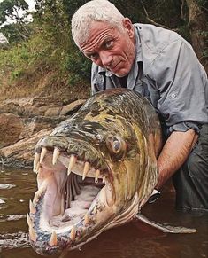 a man holding a large fish with its mouth open and teeth out in the water