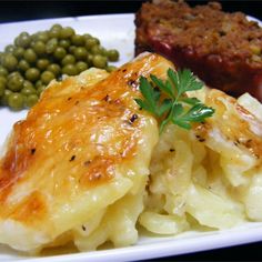 a white plate topped with macaroni and cheese covered in sauce next to green peas