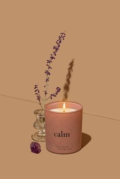 a pink candle sitting next to a glass vase filled with purple flowers on top of a table