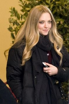 a woman with long blonde hair wearing a black coat and holding a cell phone in her hand