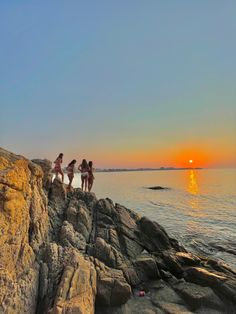 three girls are standing on the edge of a cliff by the ocean at sunset or sunrise