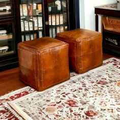 two brown leather ottomans sitting on top of a rug in front of a book case