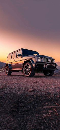 a jeep is parked on the side of a dirt road at sunset with mountains in the background