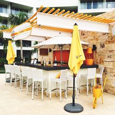 an outdoor bar with yellow umbrellas and white chairs