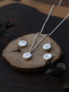 three silver necklaces sitting on top of a piece of wood next to a plant