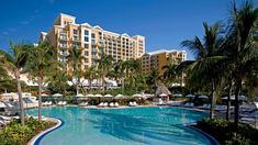 an outdoor swimming pool with lounge chairs and palm trees surrounding it in front of a hotel