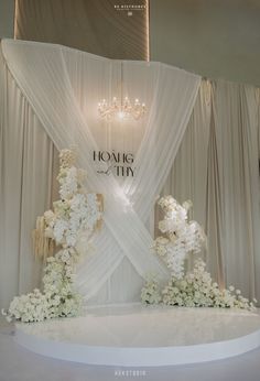 a wedding cake with white flowers and chandelier hanging from the ceiling in front of a backdrop