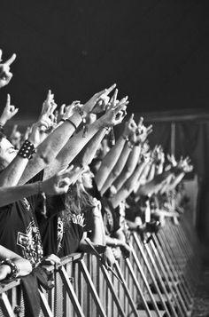 a group of people standing next to each other in front of a metal fence holding their hands up