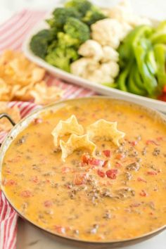 a bowl of soup with tortilla chips and broccoli in the background