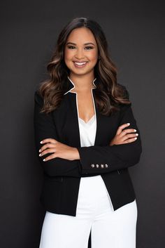 a woman in white pants and black jacket posing for the camera with her arms crossed