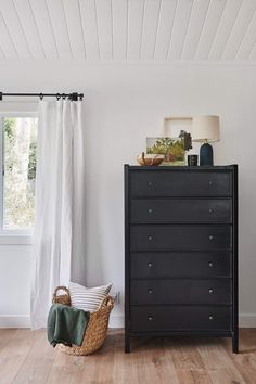 an empty room with a black dresser and white curtains