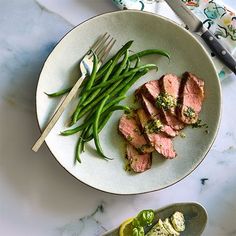 a white plate topped with meat and green beans next to a bowl of broccoli