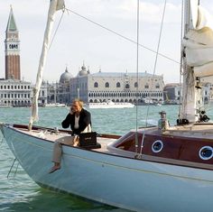 a woman sitting on top of a sailboat in the water next to a large building