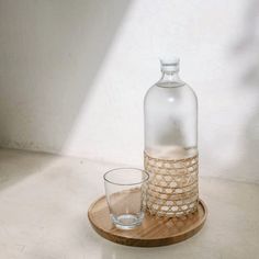 a glass and bottle sitting on a wooden tray next to each other in front of a white wall