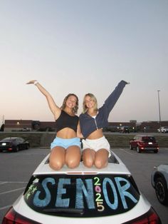 two women sitting on the back of a white car with their arms in the air