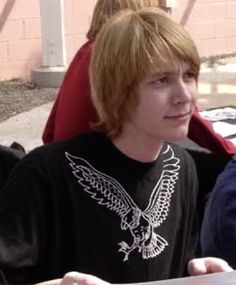 a young man sitting at a table with an eagle t - shirt on and looking off to the side