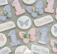 decorated cookies are arranged on a table with name tags and butterflies in pastel colors