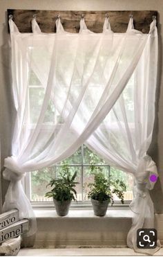 a window with white curtains and potted plants