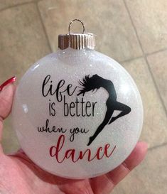 a hand holding a glass ornament that says life is better when you dance