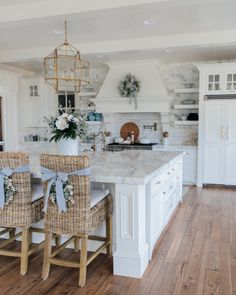 two wicker chairs sit at the center of a kitchen island with marble countertops and white cabinets