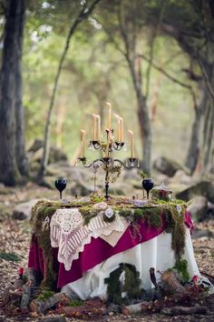 a table covered in moss with candles and decorations on it, surrounded by rocks and trees