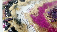 an abstract painting with purple and gold glitters on the ground, including black rocks