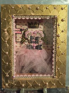 a gold frame with a pink tutu skirt and tiara on it, in front of a blue wall