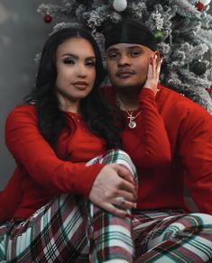 a man and woman sitting in front of a christmas tree wearing matching red sweaters