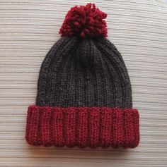 a knitted beanie with a red and gray pom - pom on top