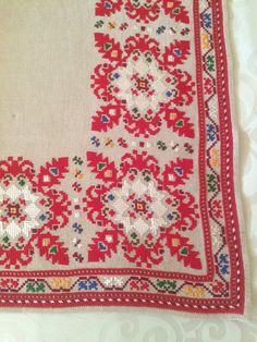 a red and white embroidered cloth with floral designs on it's edges, sitting on a table