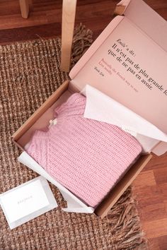 a pink sweater in a box on the floor next to a cardigan and envelope