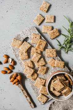 crackers and nuts on a table next to a bowl of almonds with rosemary sprigs