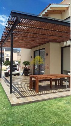 a wooden bench sitting under a pergolan covered patio area in front of a house