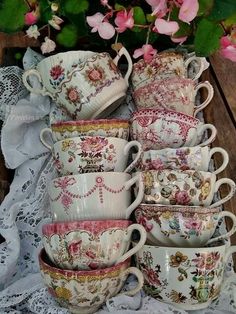 there are many cups and saucers on the table next to each other with pink flowers in the background