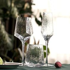 three wine glasses sitting on top of a table next to a plate with an apple